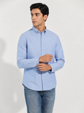 Model wearing Cauzeway chambray blue Oxford shirt, adjusting cuff, close view.