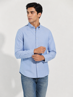 Model wearing Cauzeway chambray blue Oxford shirt, adjusting cuff, close view.