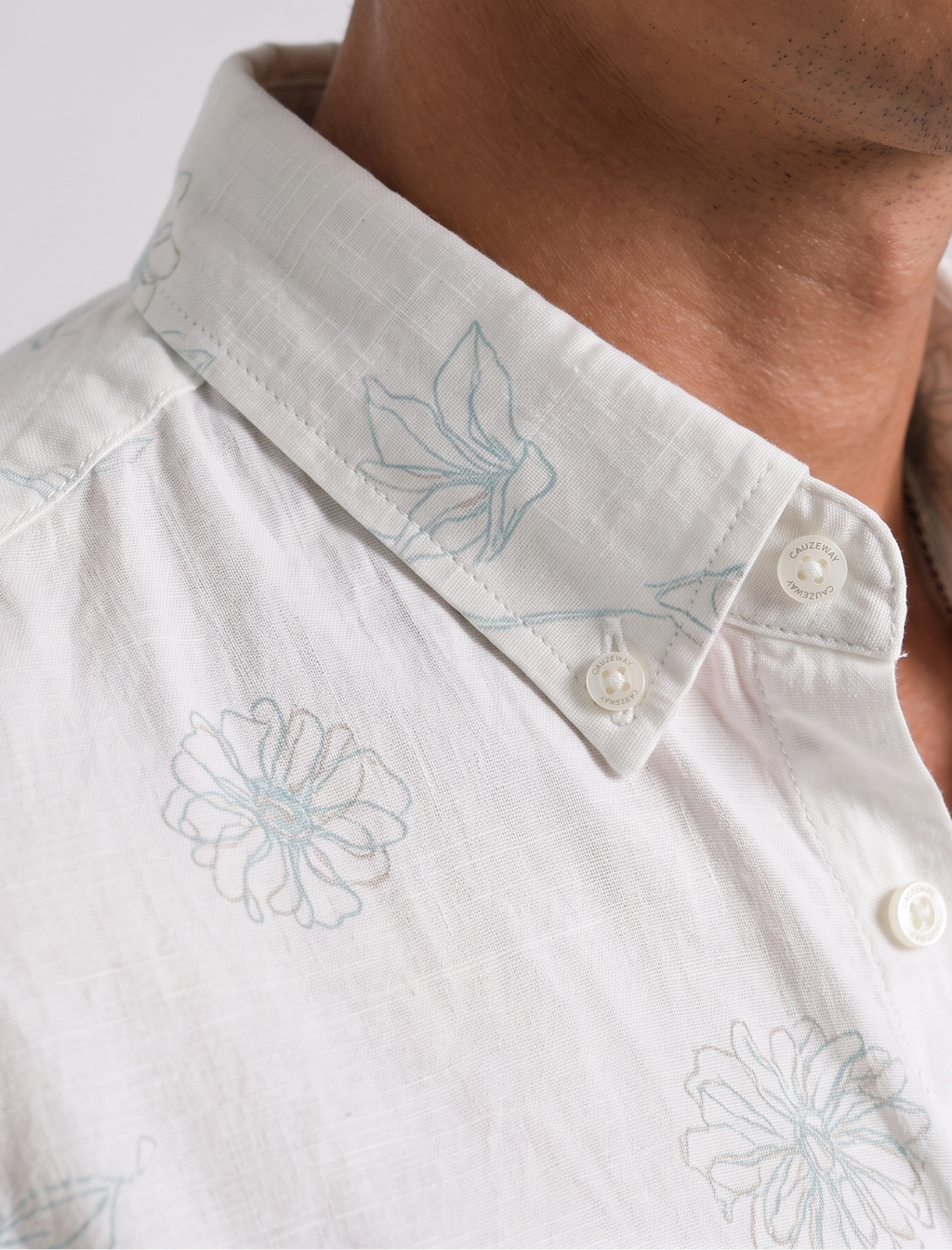 Close up of the button-down collar with Cauzeway branded buttons on white floral print shirt