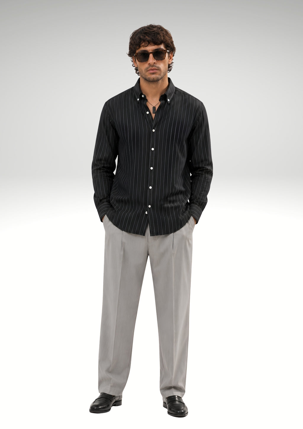 Model wearing Cauzeway black pinstripe shirt engineered for the Indian body type, styled casually and untucked with grey trousers.